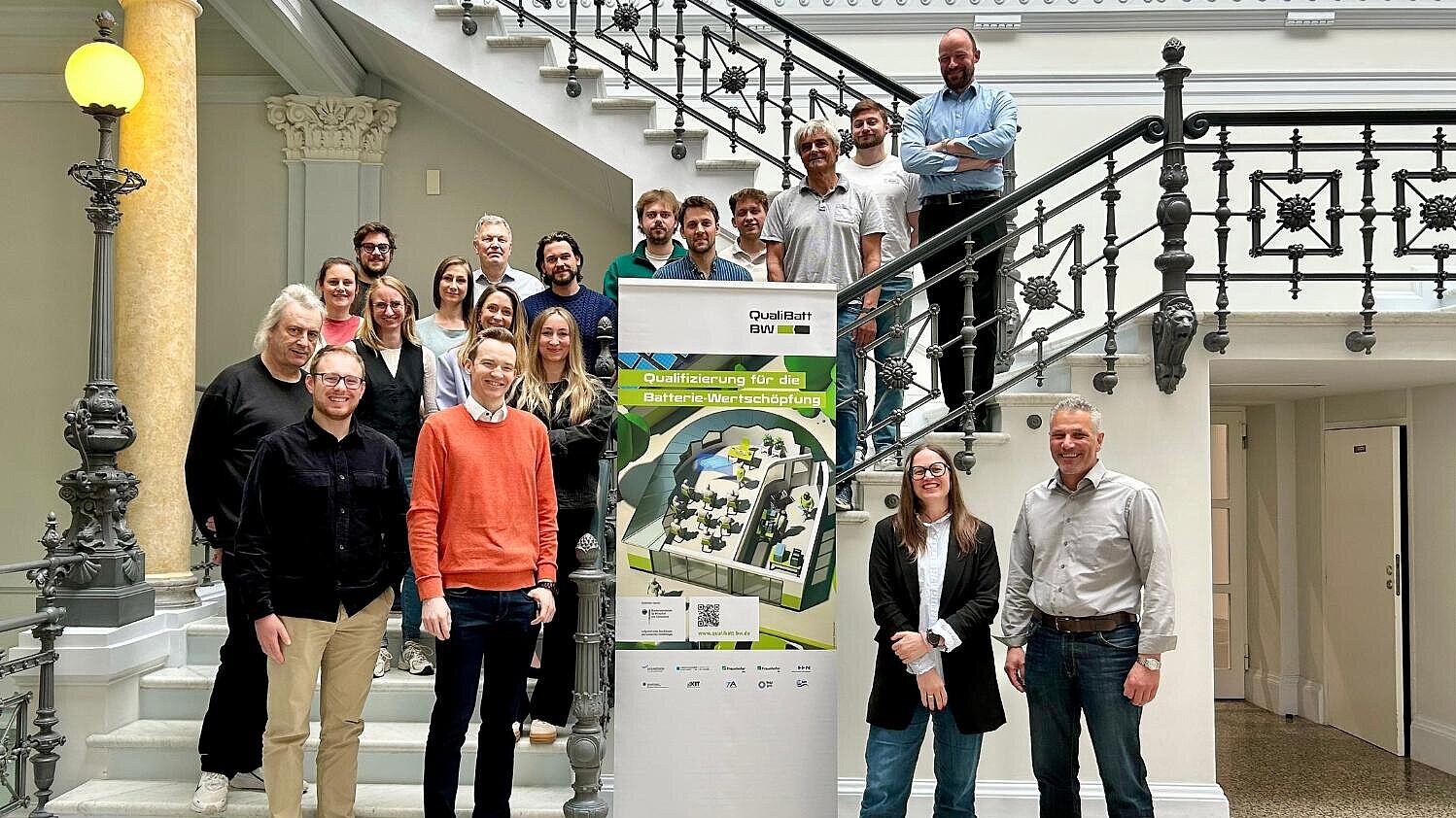 Eine Gruppe von Personen steht vor einem Roll-up des Projektes QualiBattBW.