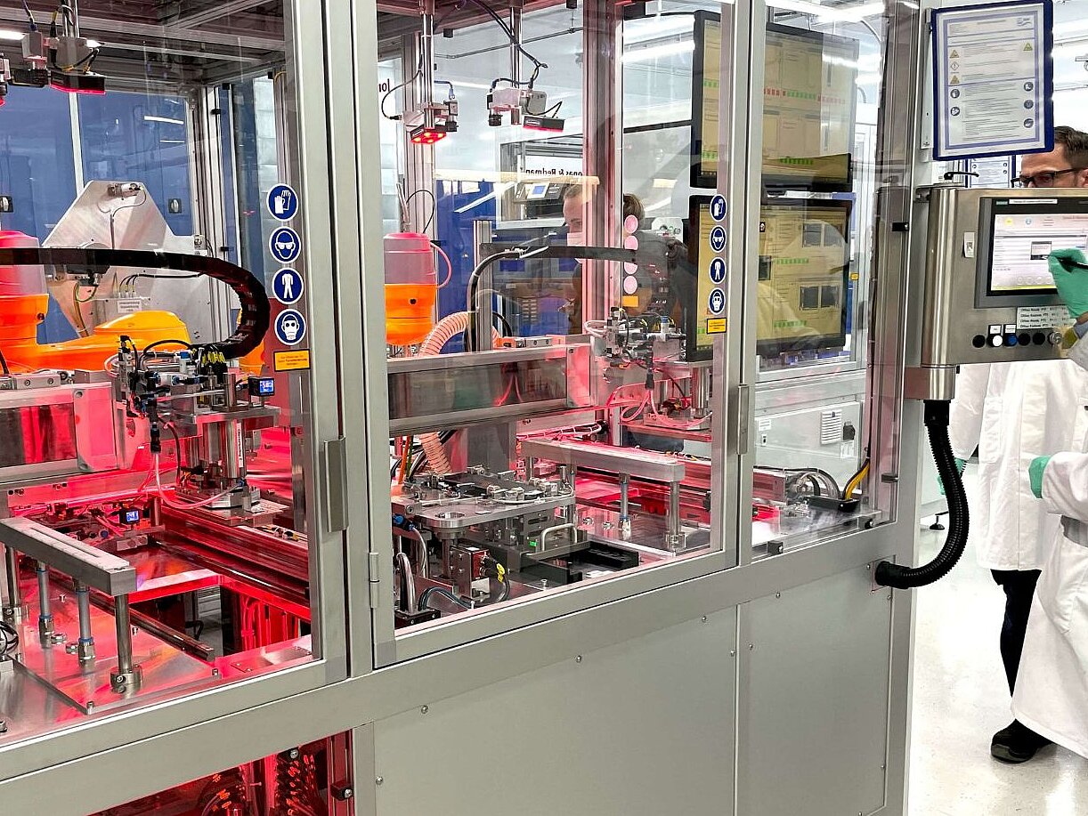 Forschende in weißem Laborkittel überwachen automatisierte Fertigung von Batteriesystemen in Laborumgebung.