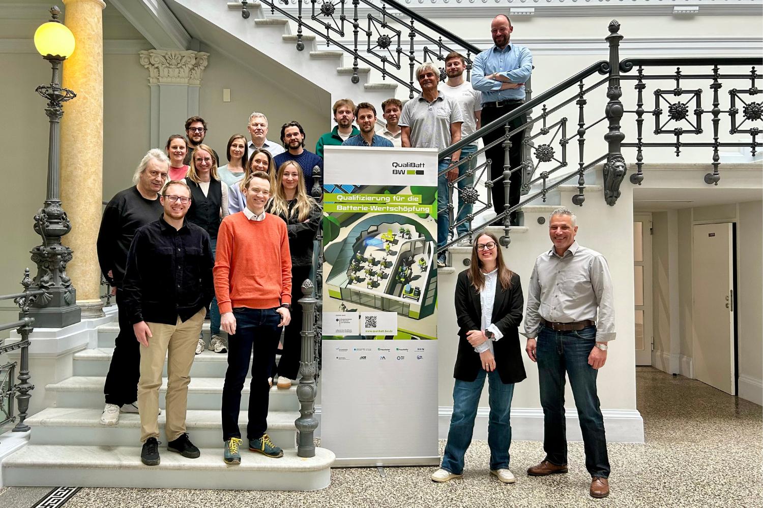 Eine Gruppe von Personen steht vor einem Roll-up des Projektes QualiBattBW.